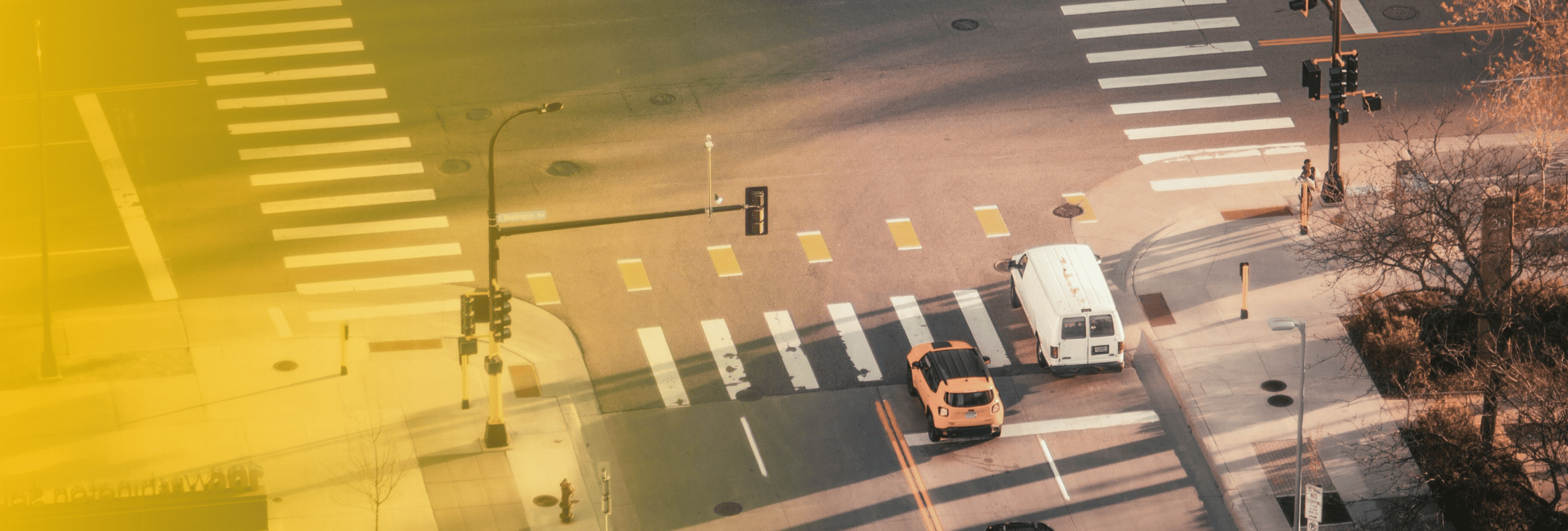 Intersection with cars stopped at a red light and visible pedestrian crosswalks.